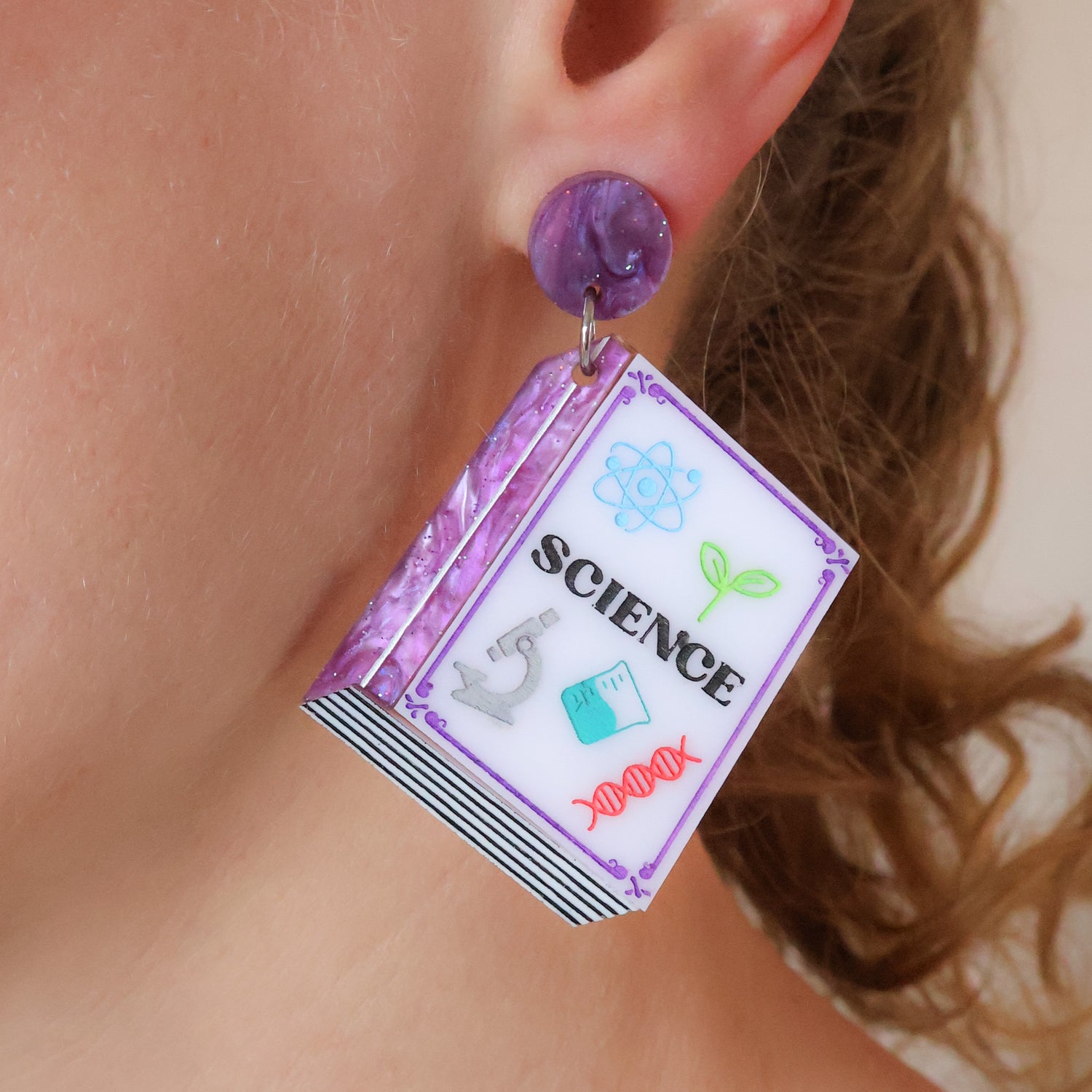 Purple toned Textbook shaped earrings with 'SCIENCE' title worn by a person