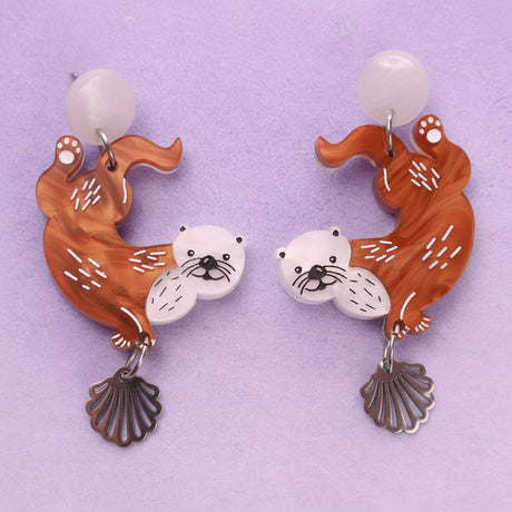 A pair of acrylic earrings with sea otter design on a light blue background