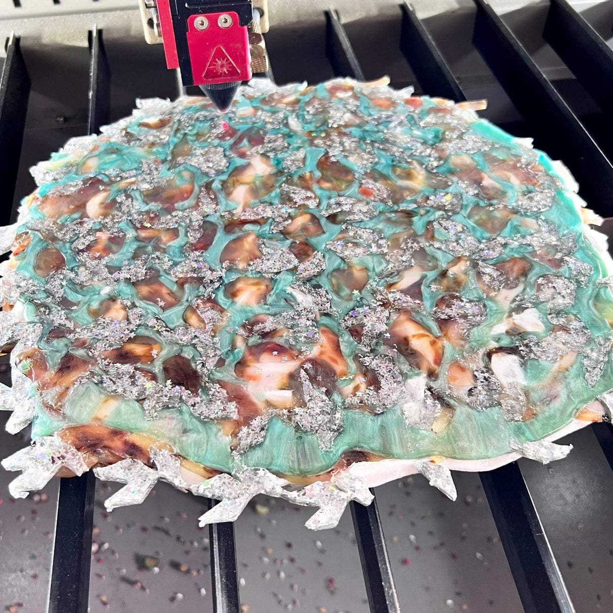 A melt pressed recycled acrylic sheet showing a randomised assortment of green  silver and brown coloured acrylic scraps pressed within.