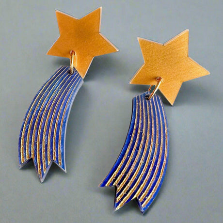 Shooting star earrings, comprised of gold toned acrylic star toppers with blue and gold star trails dangling underneath.