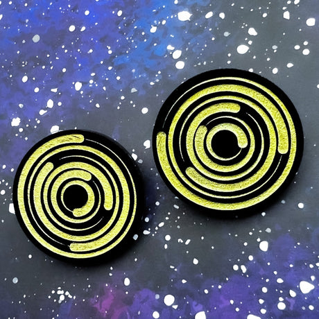 A pair of round acrylic star trail studs, black with gold painted star trails within.