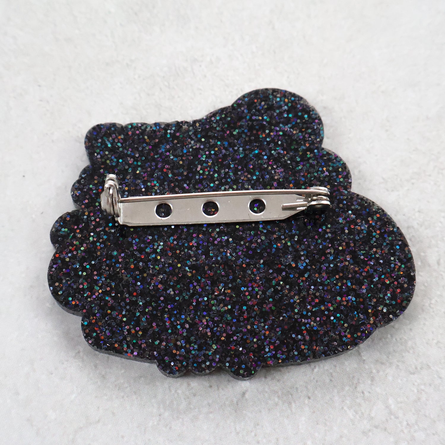 Black glittery brooch back view with a stainless steel brooch pin and rolling clasp.