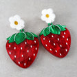 Strawberry-shaped acrylic earrings with white flower toppers on a gray background