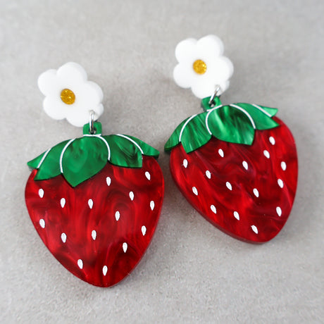 Strawberry-shaped acrylic earrings with white flower toppers on a gray background