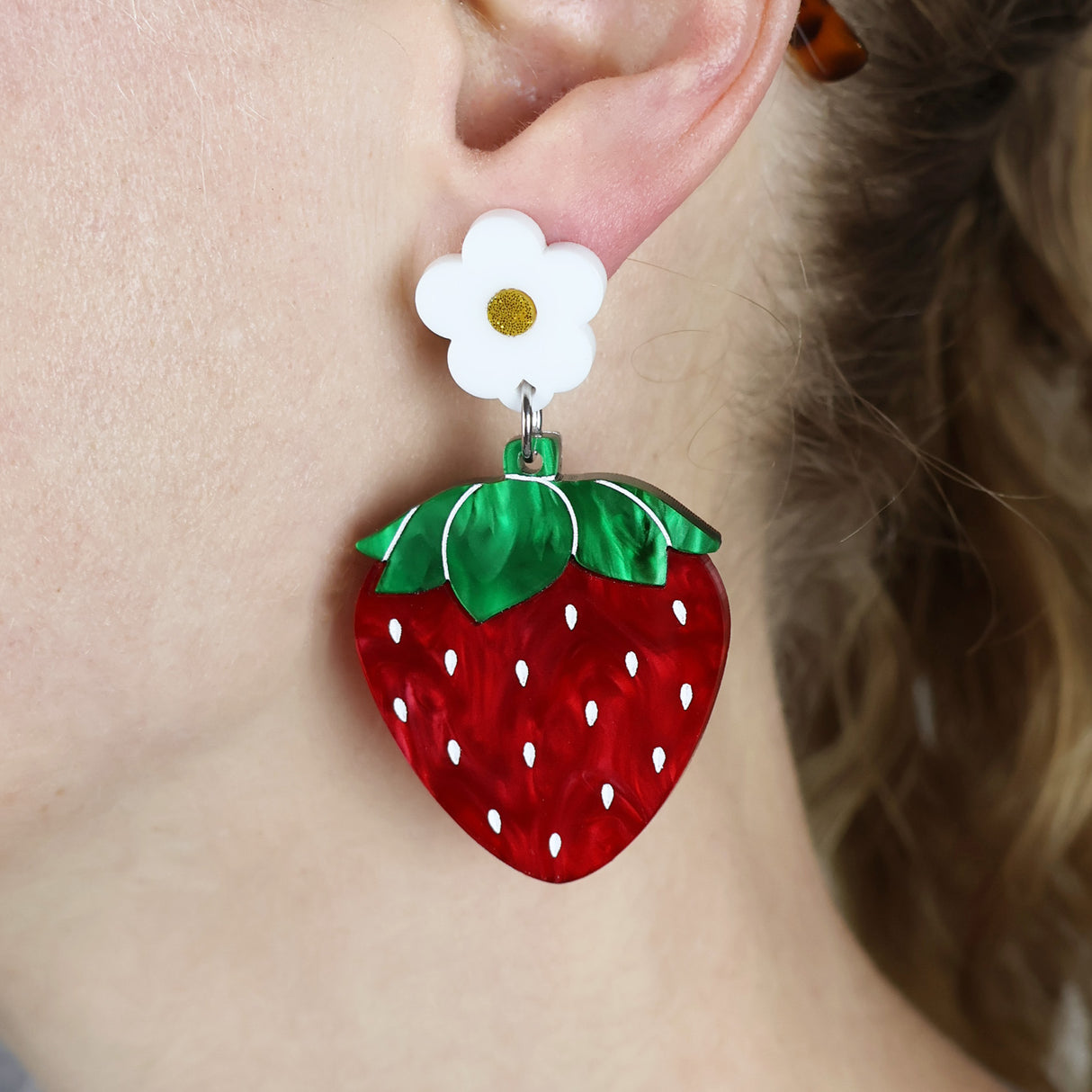 Strawberry-shaped acrylic earrings with a white flower topper on an ear.