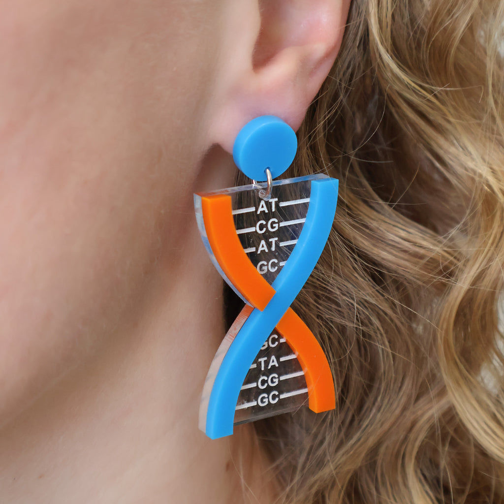 A pair of DNA earrings in blue and orange tones, handmade from laser cut acrylic, and being modelled.