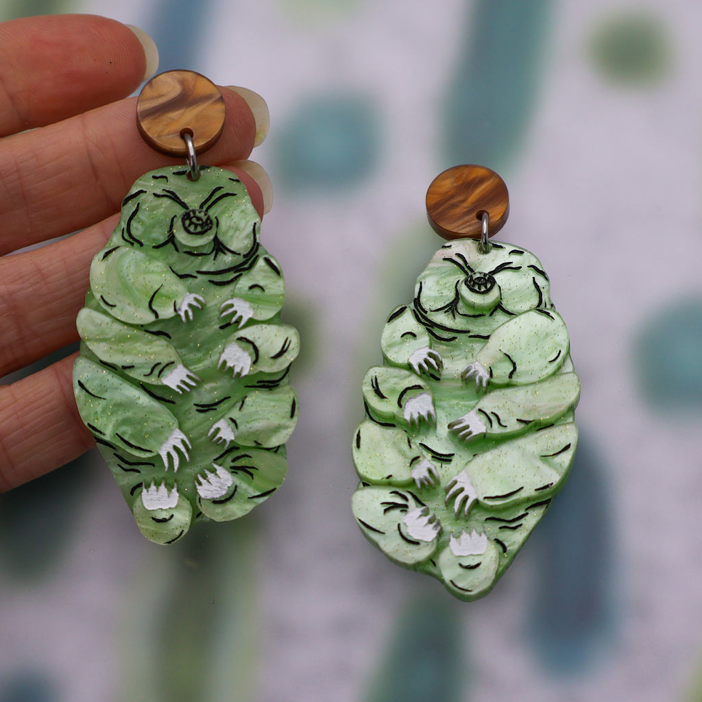 Tardigrade earrings made from swirly apple green acrylic, hanging from swirly brown round earring toppers.