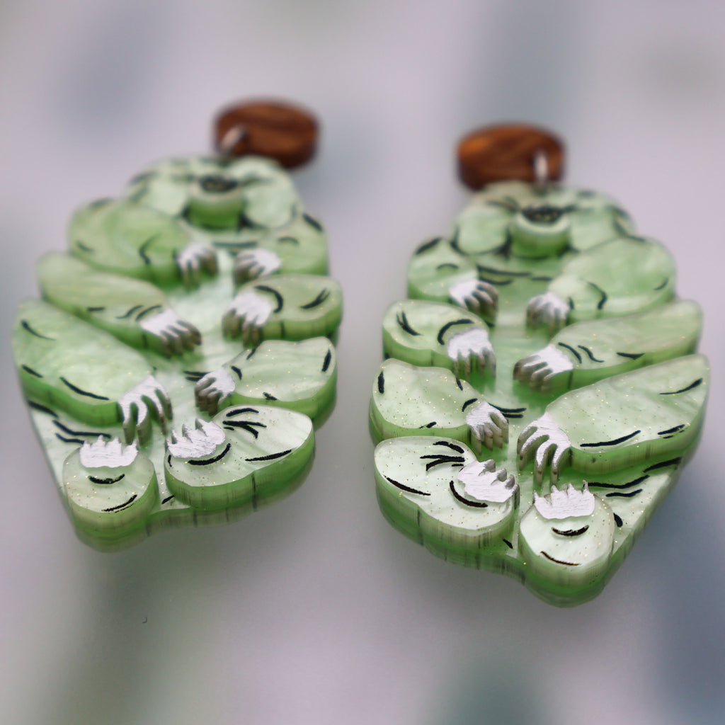 Angled view of Tardigrade earrings made from swirly apple green acrylic, hanging from swirly brown round earring toppers.