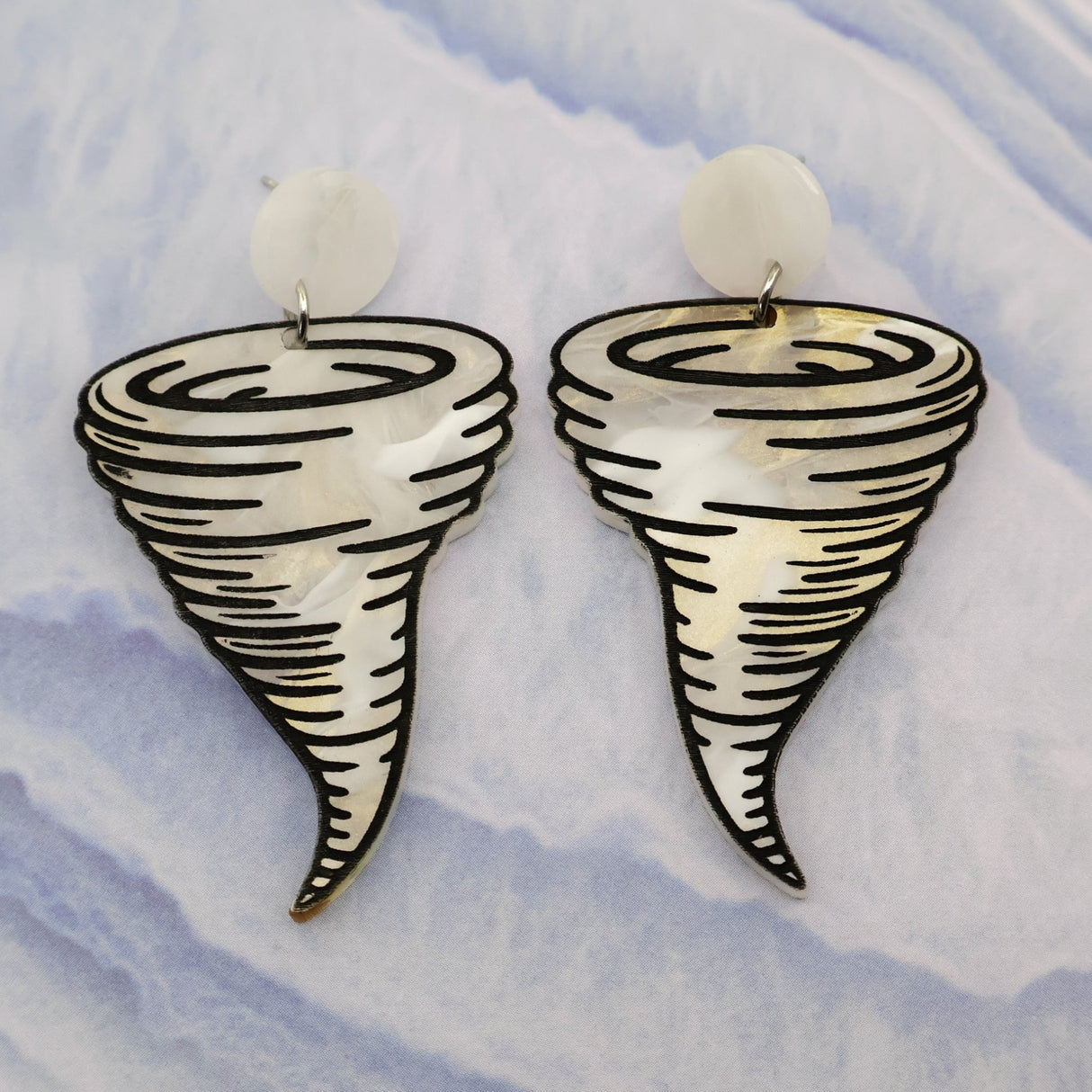 Tornado-shaped acrylic dangle earrings on a light blue and white marbled background