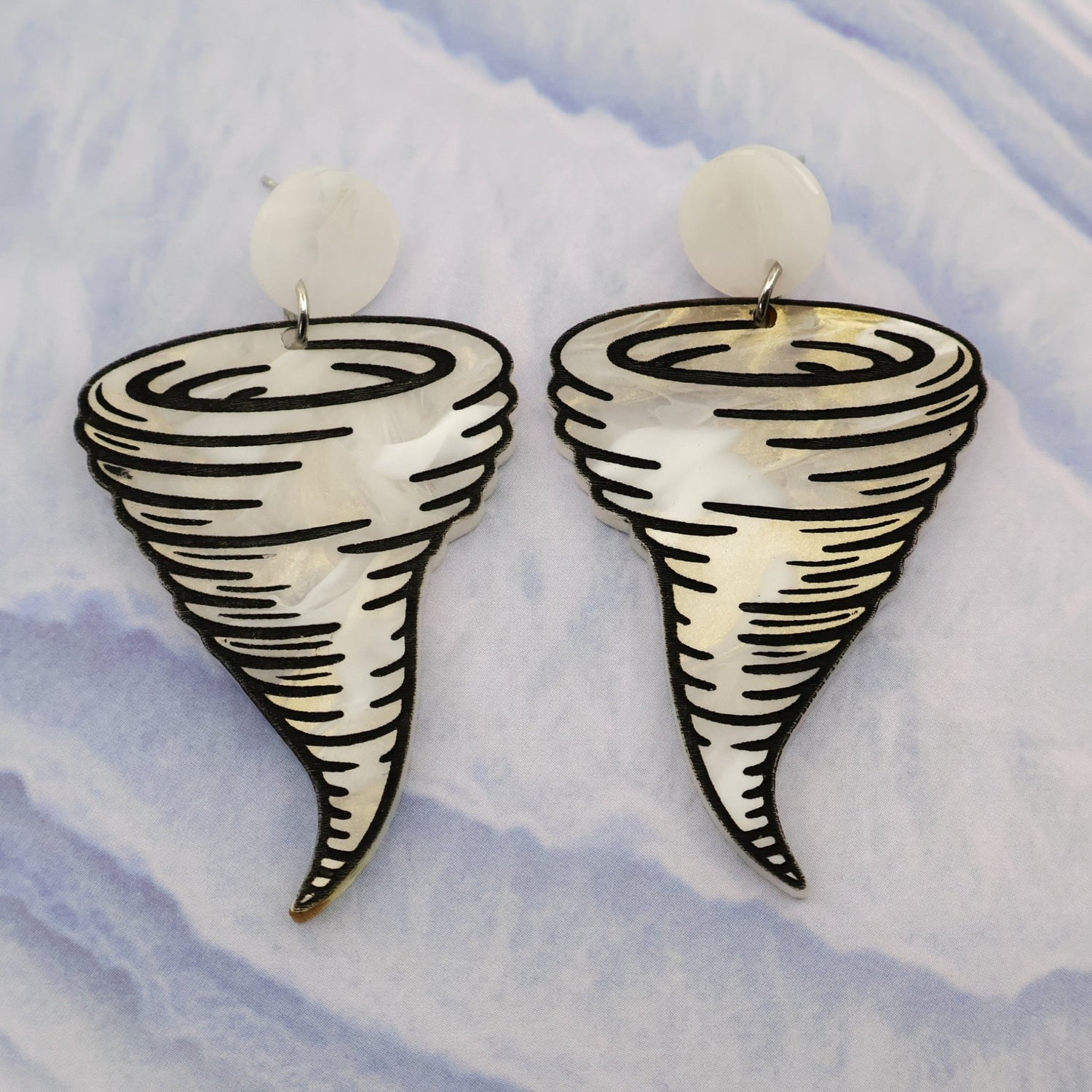 Tornado-shaped acrylic dangle earrings on a light blue and white marbled background