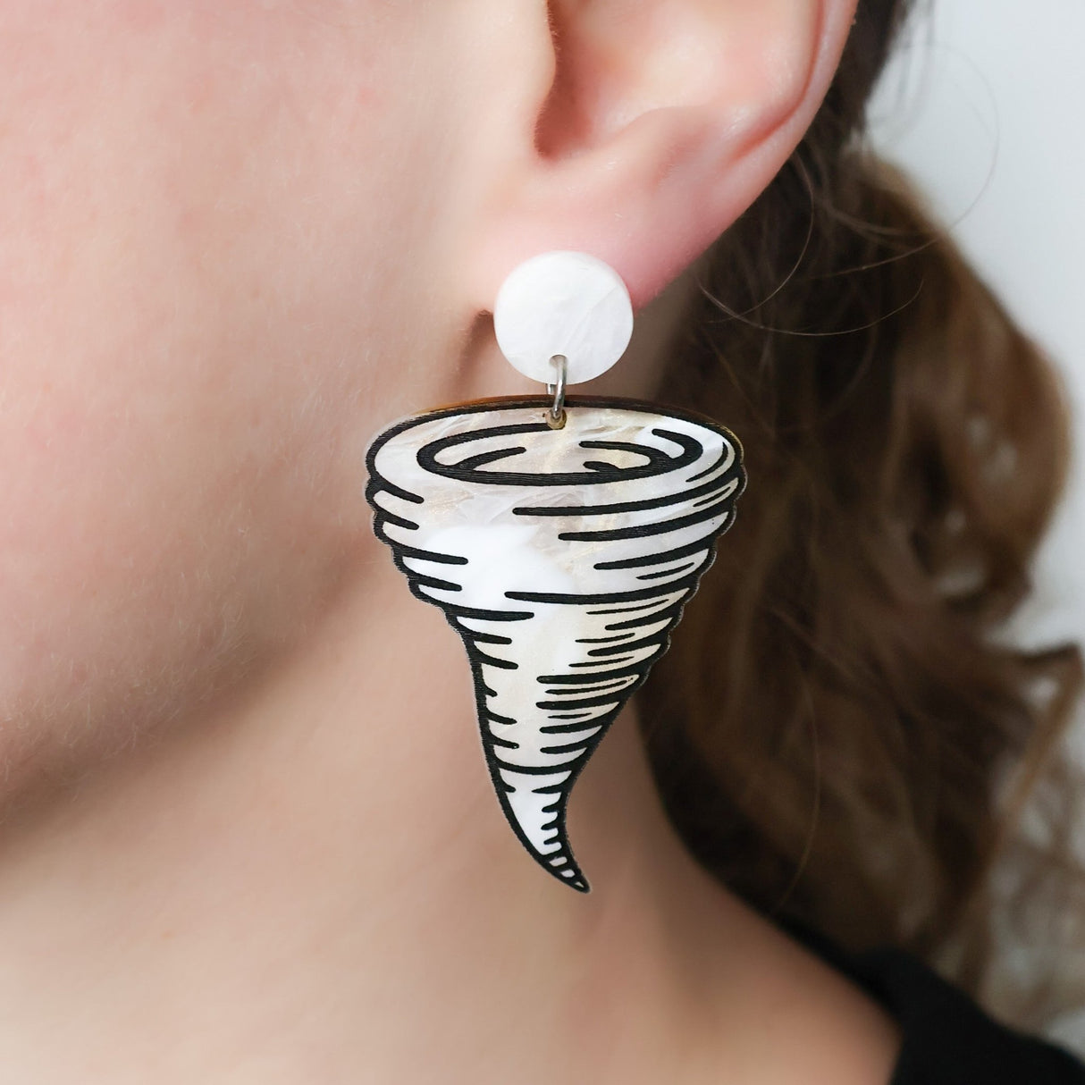 Tornado shaped laser cut acrylic dangle earrings with round acrylic toppers, being modelled on an ear.