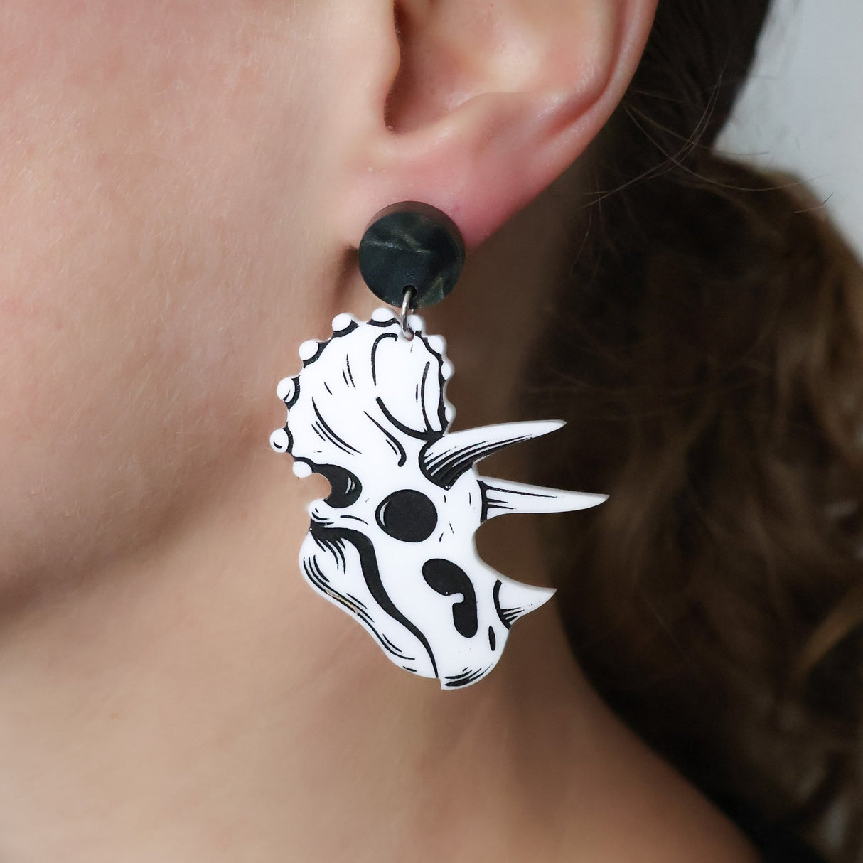 Close-up of a person wearing a black and white triceratops skull dangle acrylic earring.