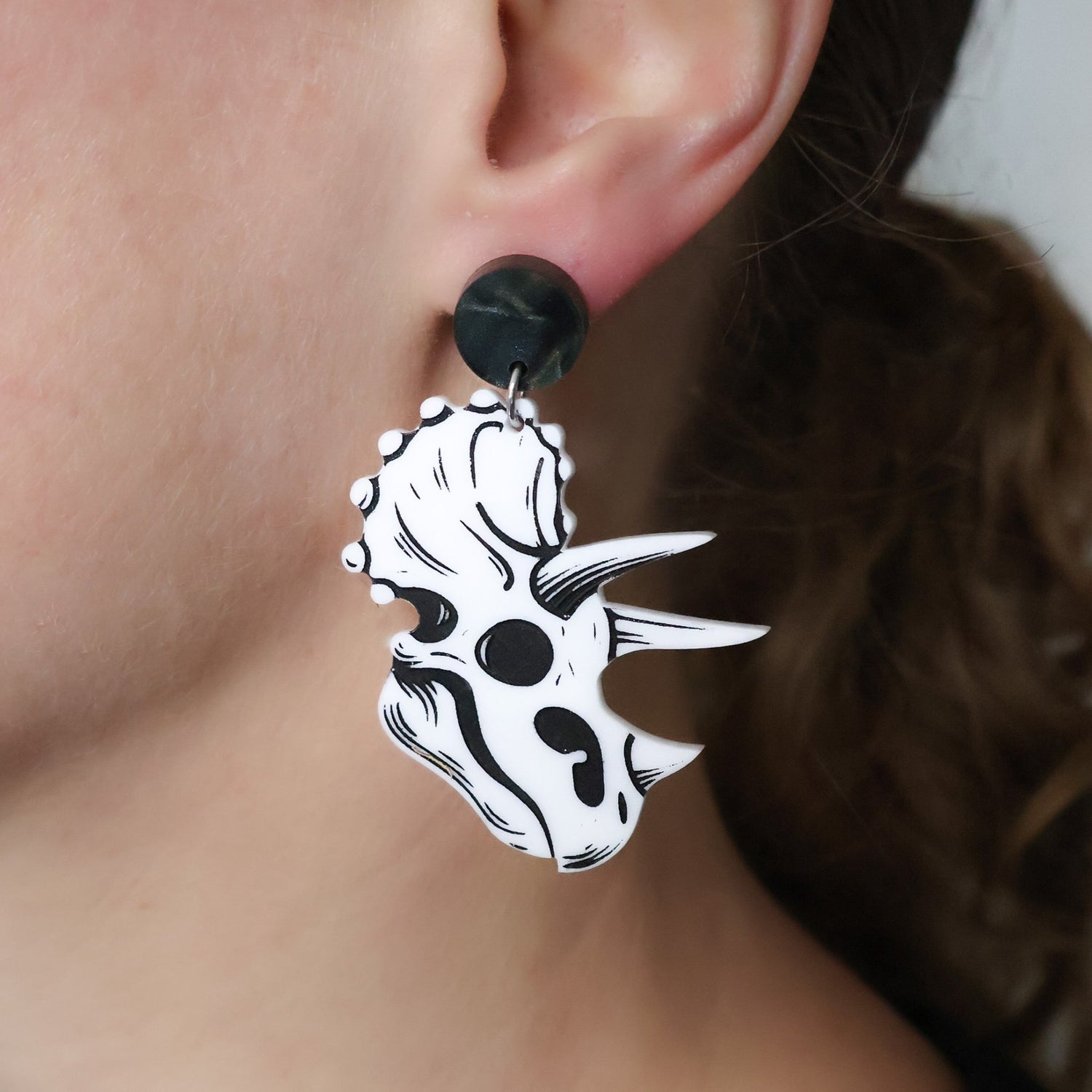 Close-up of a person wearing a black and white triceratops skull dangle acrylic earring.