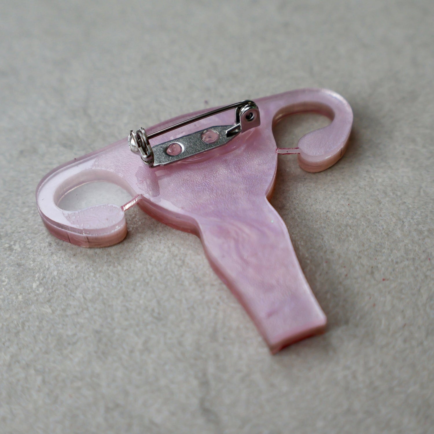 The back view of a laser cut acrylic uterus brooch, showing the stainless steel brooch pin with rolling clasp.
