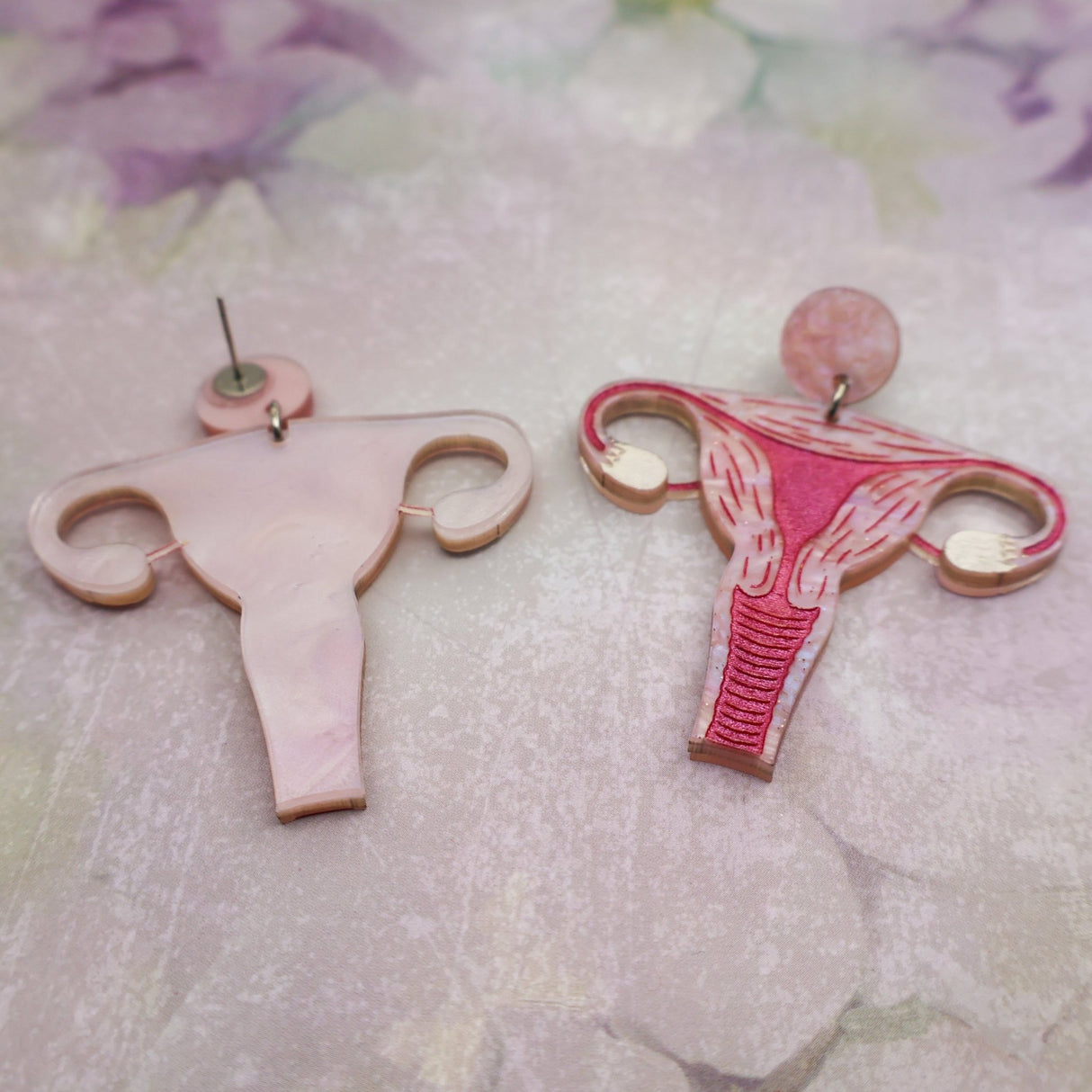 Uterus-shaped acrylic earrings on a floral background showing both the front and back views
