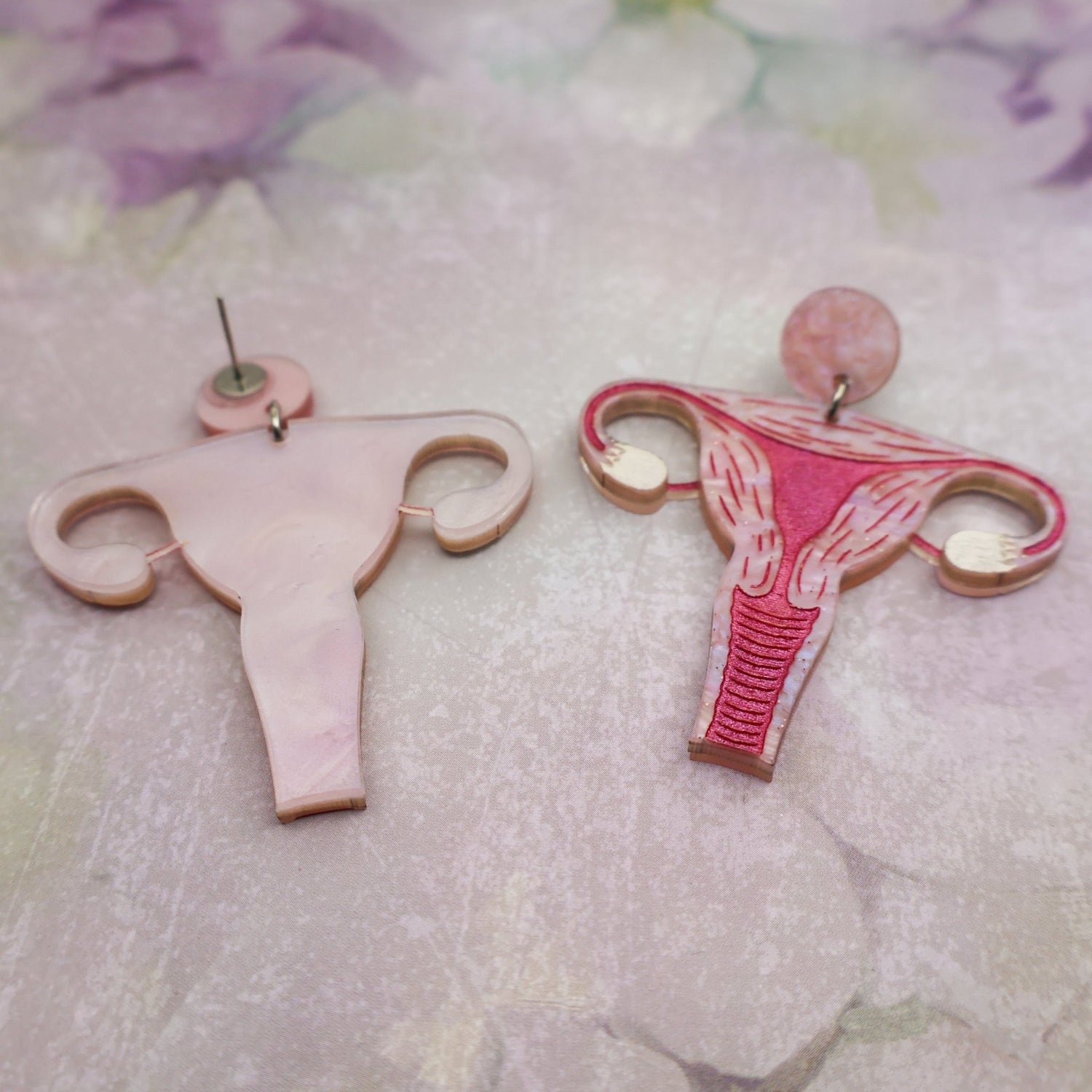 Uterus-shaped acrylic earrings on a floral background showing both the front and back views