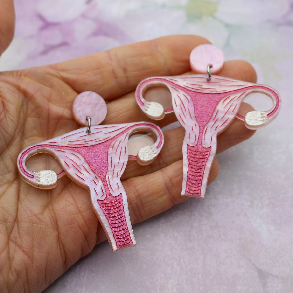 Pink acrylic uterus dangle earrings being held in a hand.