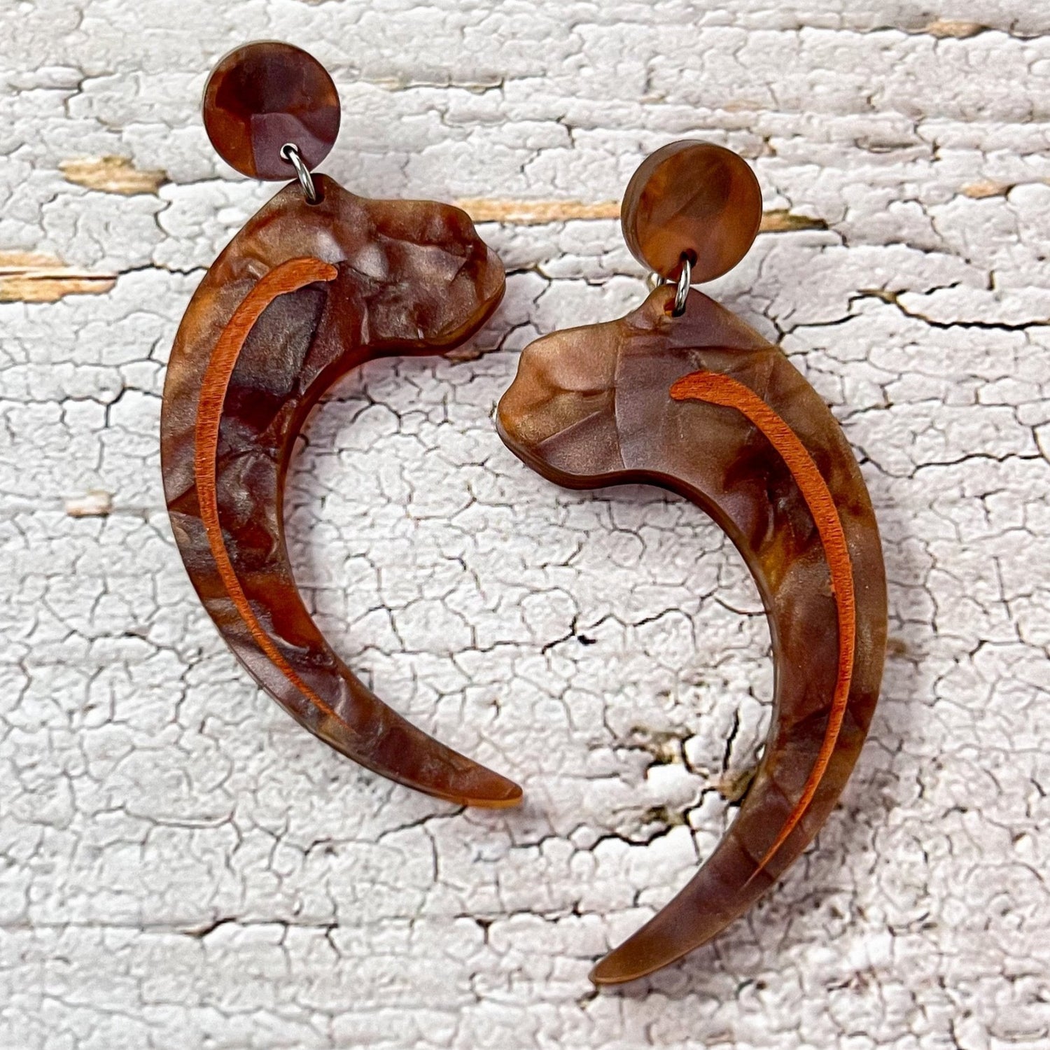 Velociraptor claw earrings, laser cut from textured brown acrylic, and hanging from brown acrylic earring toppers.