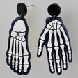 A pair of mismatched earrings, one in the shape of a hand and the other a foot, with a x-ray bone pattern on a black background.