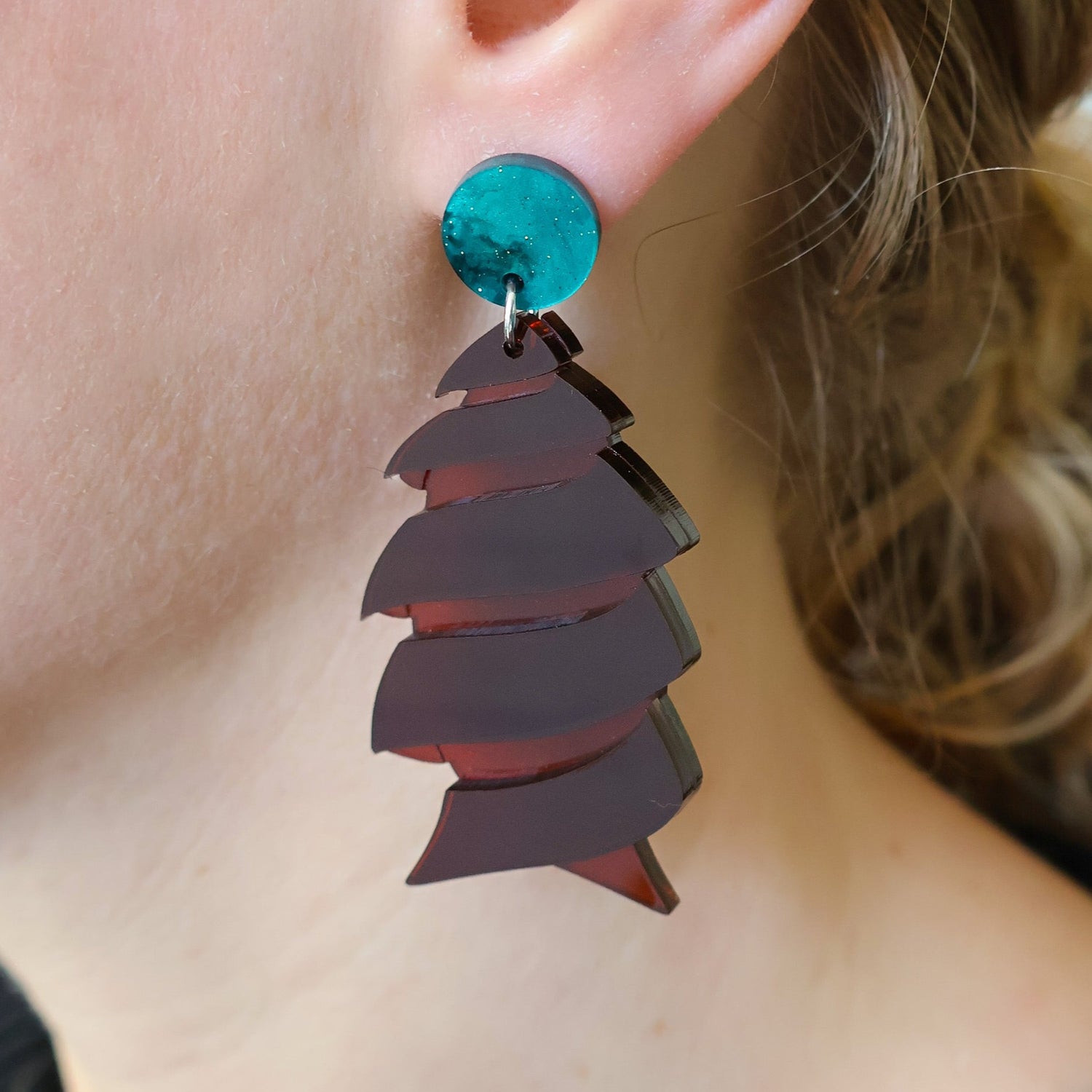 Brown acrylic cork screw shark egg earrings being modelled, showing green acrylic toppers and transparency in the broch acrylic.