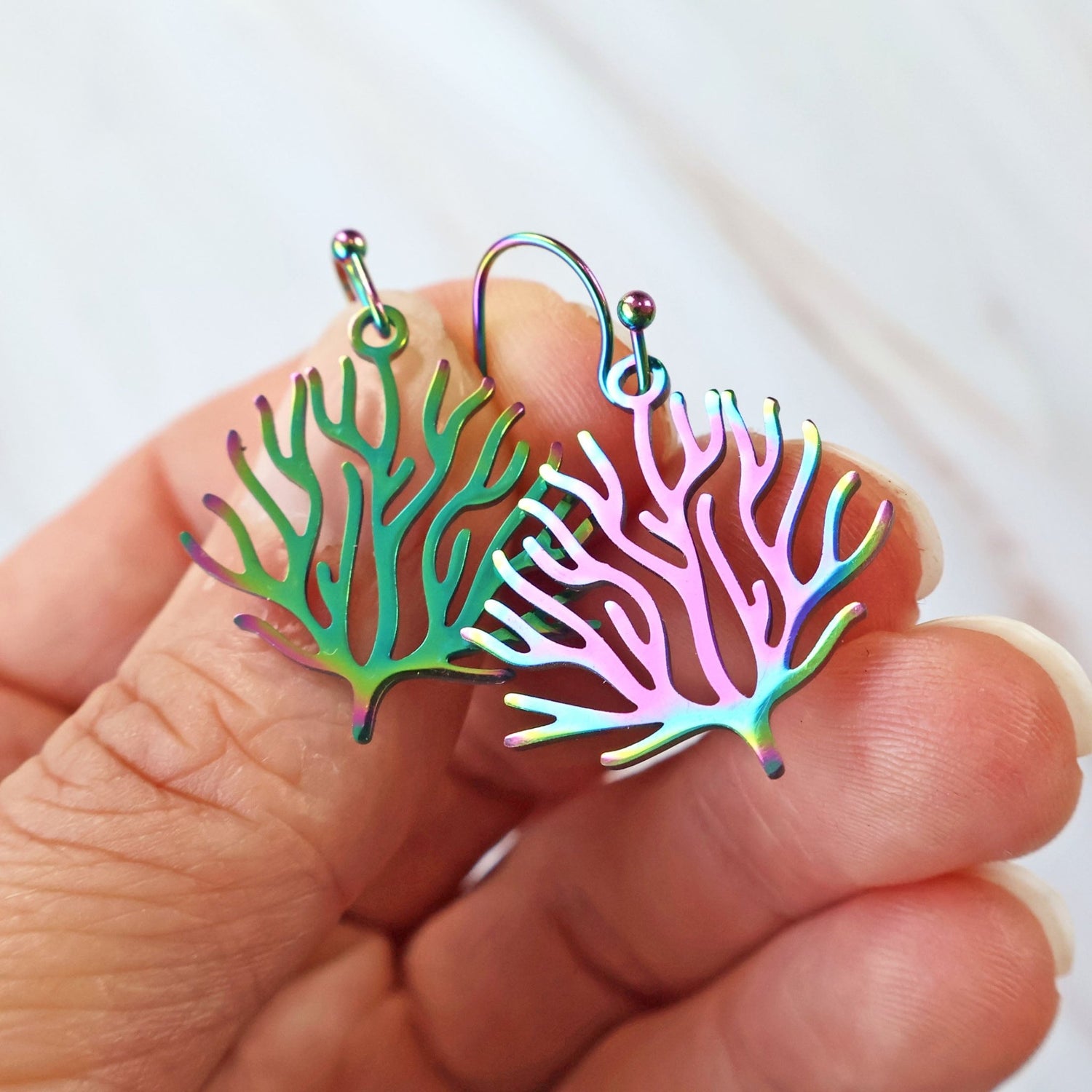 Small Colorful coral-shaped earrings held between fingers against a white background