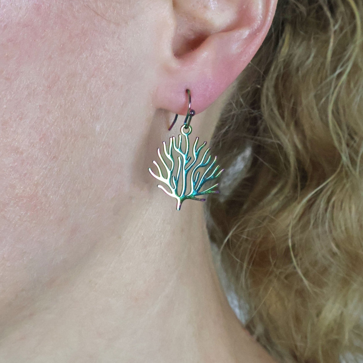 Close-up of an ear wearing small coral  shaped dangle earrings with french hook tops.
