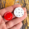 A pair of asymmetrical studs. One side is a red blood cell while the other side is a larger white blood cell. Laser cut, and handpainted from acrylic.