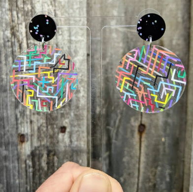Clear circle earrings with multicoloured circult designs painted on back and front, and hanging from black glittery earring toppers.