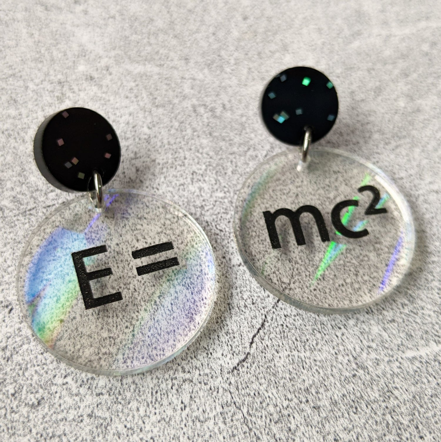 E =mc2 earrings, with black text engraved into holographic effect acrylic discs. Equation bridges both earrings. Black glitter earring toppers. Alternative view.