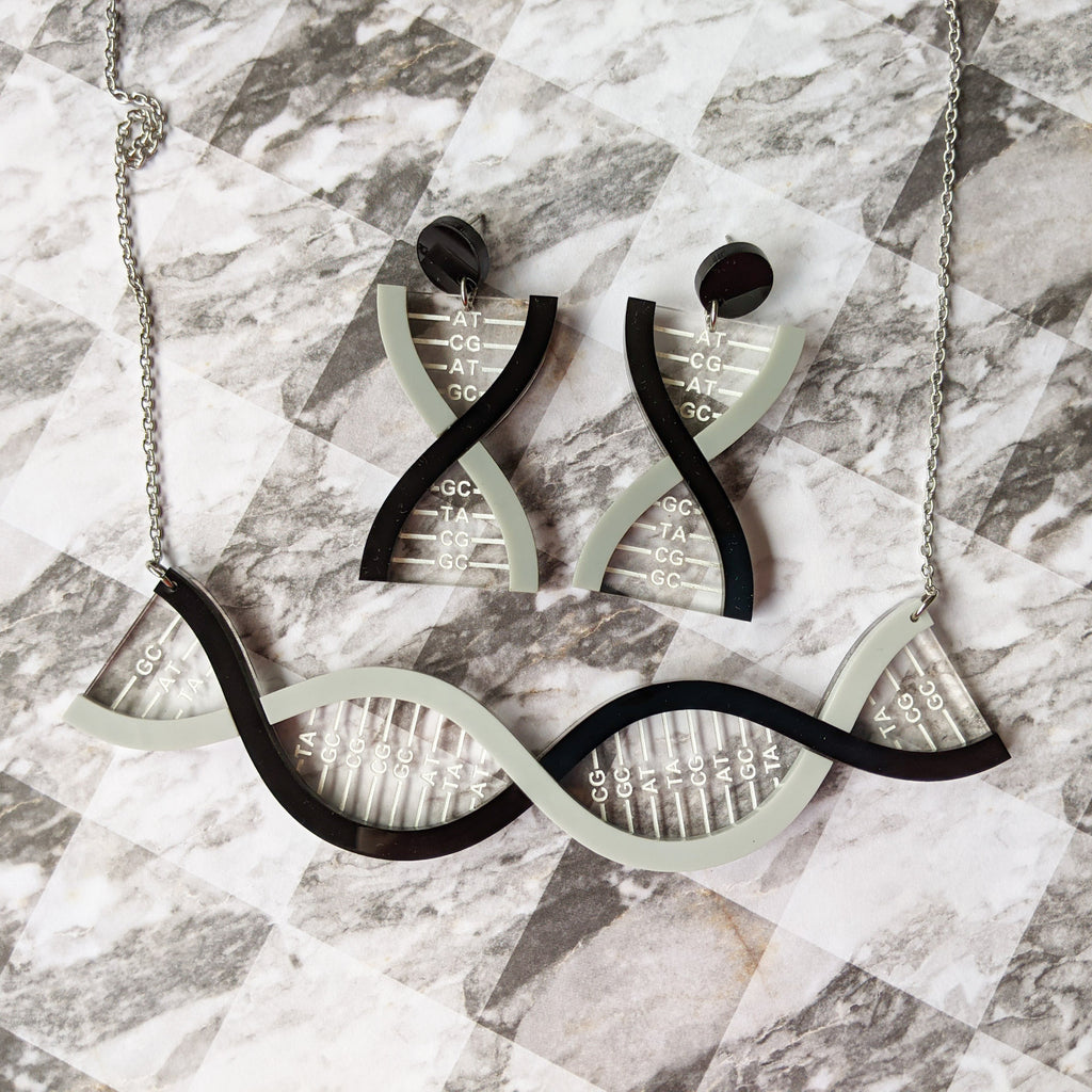 A DNA necklace and a matching pair of DNA earrings, in greyscale, handmade from laser cut acrylic.