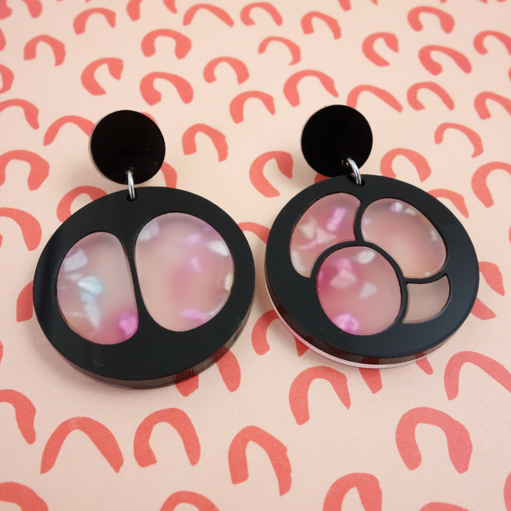 Laser Cut Acrylic Meiosis Earrings. Black and Pink Round Asymmetrical Earrings Depicting Cell Division. Closeup view.