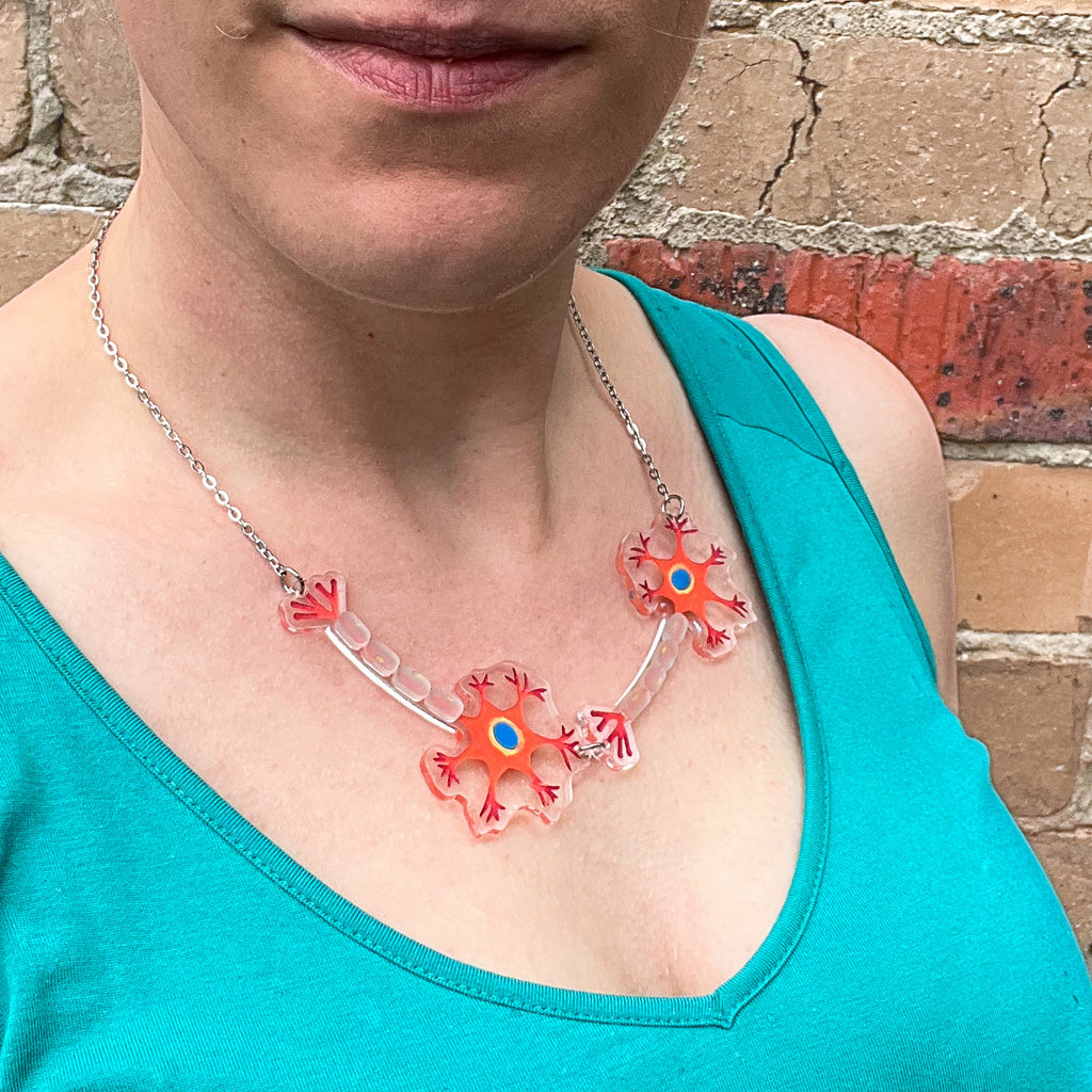A necklace comprising of two acrylic neurons with handpainted details. Laser cut from acrylic and on a stainless steel chain. Necklace is being modelled. 