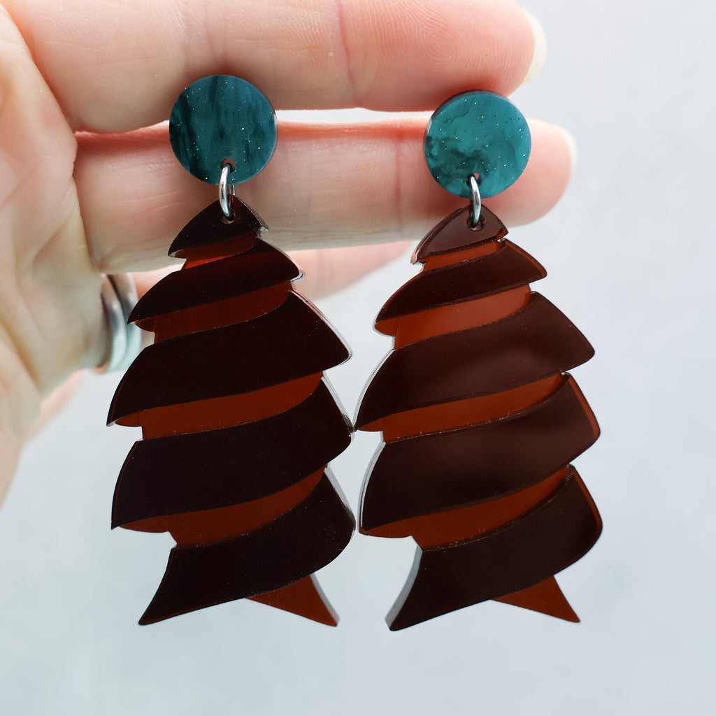 Acrylic cork-screw shark egg earrings being held up to show transparency of brown acrylic