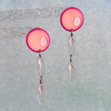 A pair of egg and sperm earrings. Two sperm dangle below a pink acrylic 'egg' topper. 