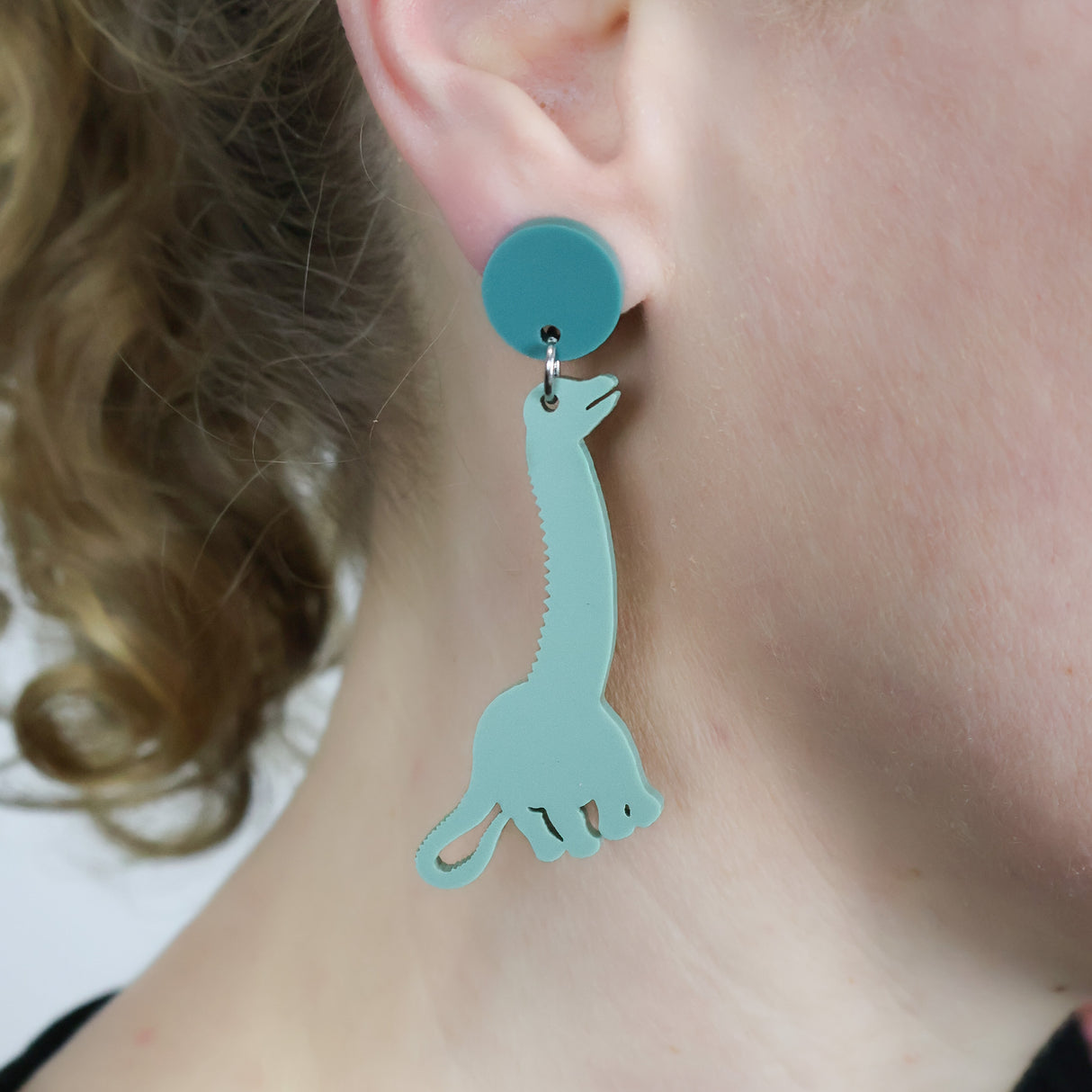 Green diplodocus dangle earrings with darker green toppers. Being modelled.