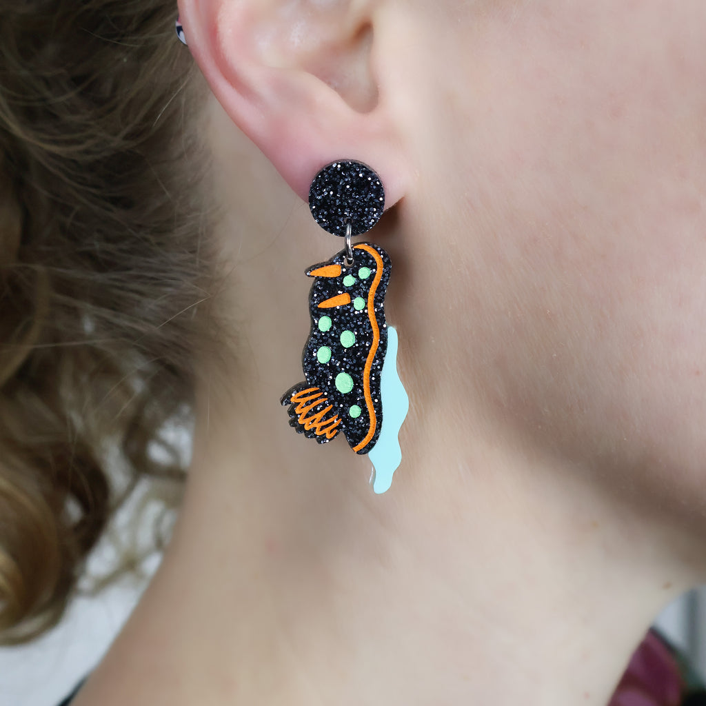 Laser cut acrylic nudibranch earrings, being modelled.