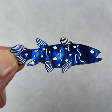 Blue coelacanth acrylic brooch being held up in hand.