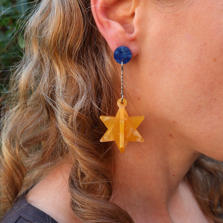 Close-up of a person wearing blue and yellow 3D star-shaped earrings.