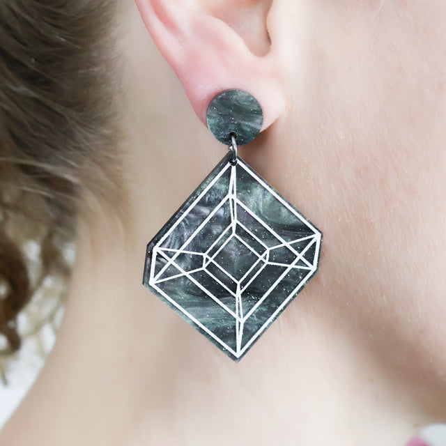 Laser cut acrylic tesseract earrings being modelled.