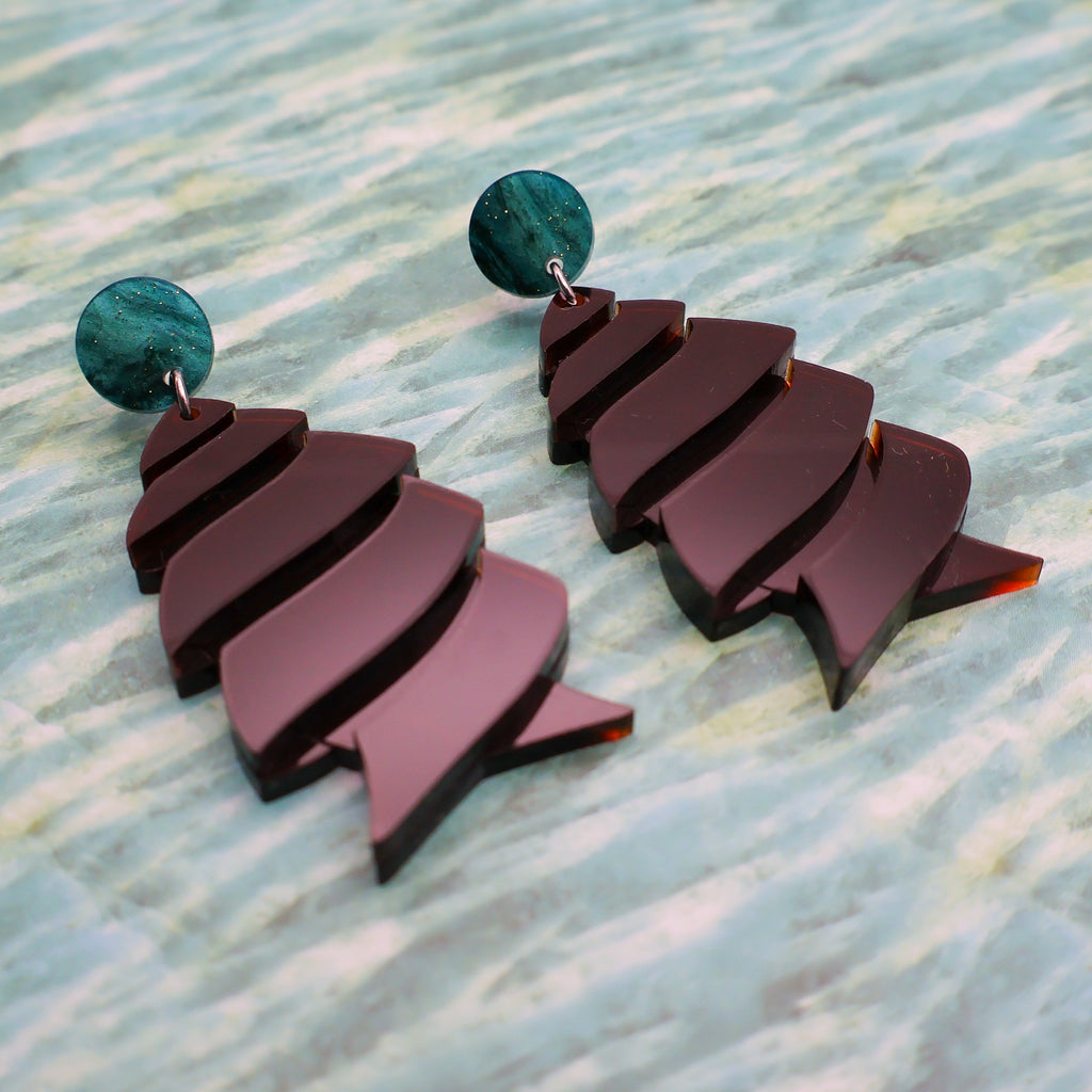 Angled view of brown cork-screw shark egg earrings with green toppers.
