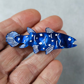 Blue coelacanth acrylic brooch being held in hand.