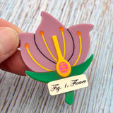 A brooch showing a cross-sectional view of a flower, with a gold Fig1: Flower label underneath. Laser cut and handpainted from acrylic.