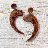 Velociraptor claw earrings, laser cut from textured brown acrylic, and hanging from brown acrylic earring toppers. 