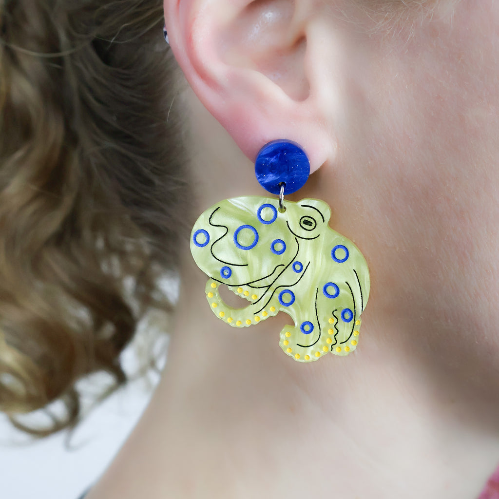 Laser cut acrylic blue ringed octopus earrings, being modelled. 