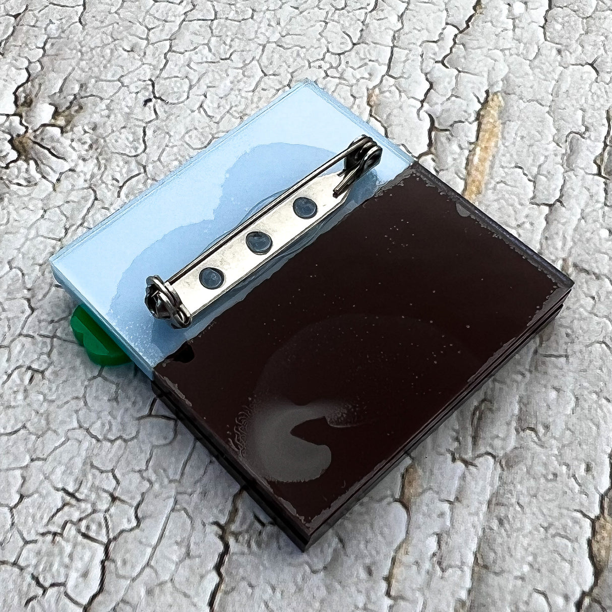 The back view of a germination acrylic brooch, showing the stainless steel brooch pin and rolling clasp. 