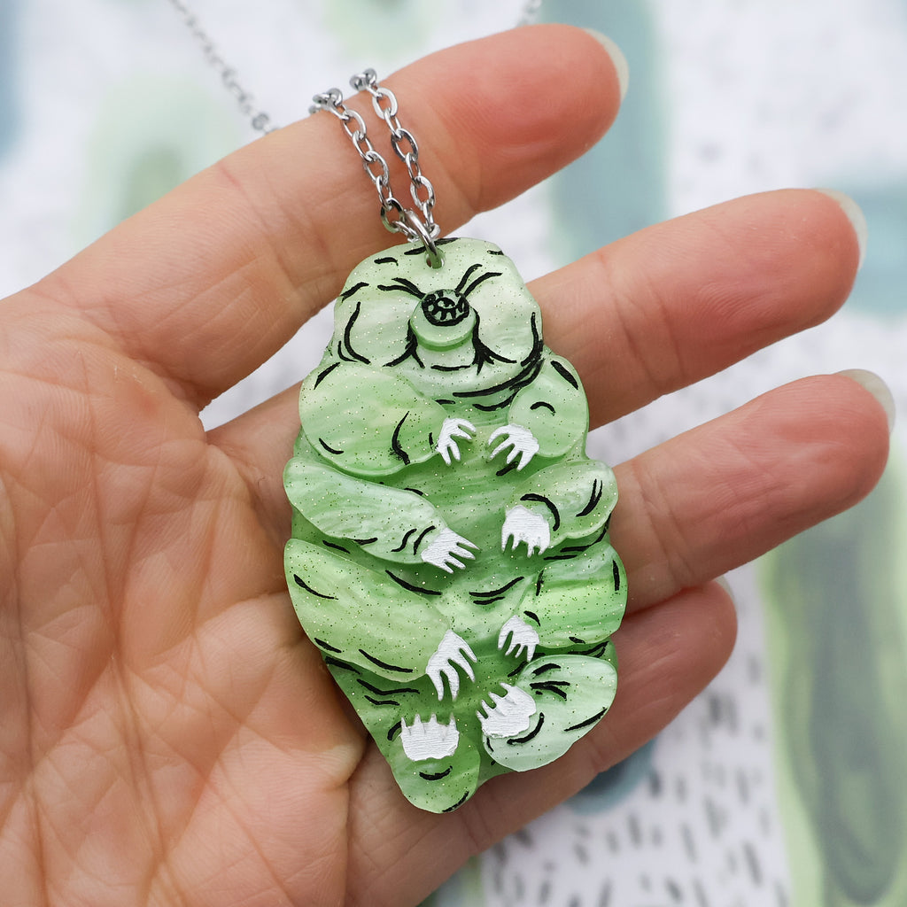Closeup of green acrylic tardigrade necklace in hand for scale