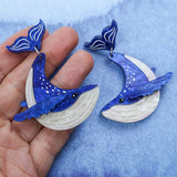 Laser cut acrylic humpback whale earrings being held in hand.