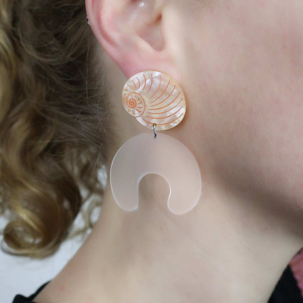 Moon snail shell and egg acrylic laser cut earrings. Being modelled.