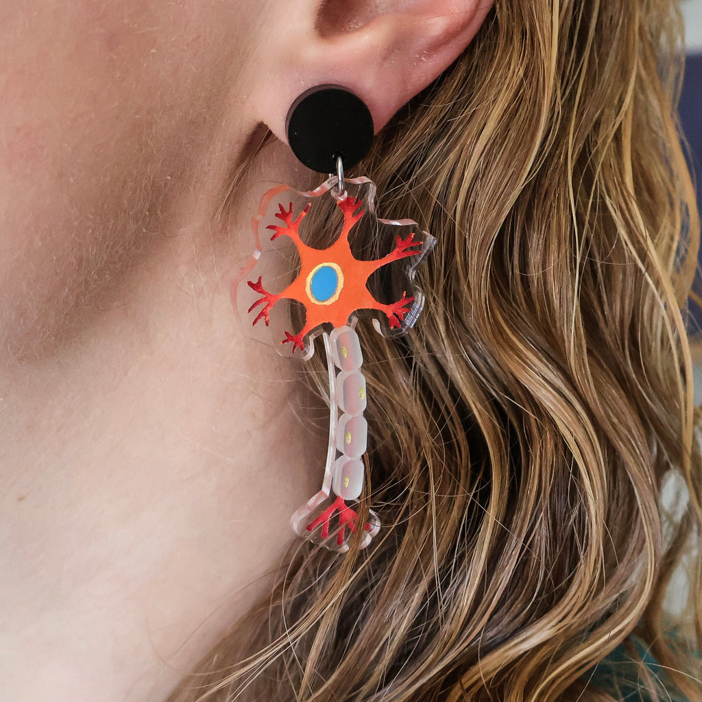 Laser cut acrylic neuron earrings being modelled. Earrings are cut from transparent acrylic, with the neuron design engraved and handpainted. The neurons hang from black earring toppers. 