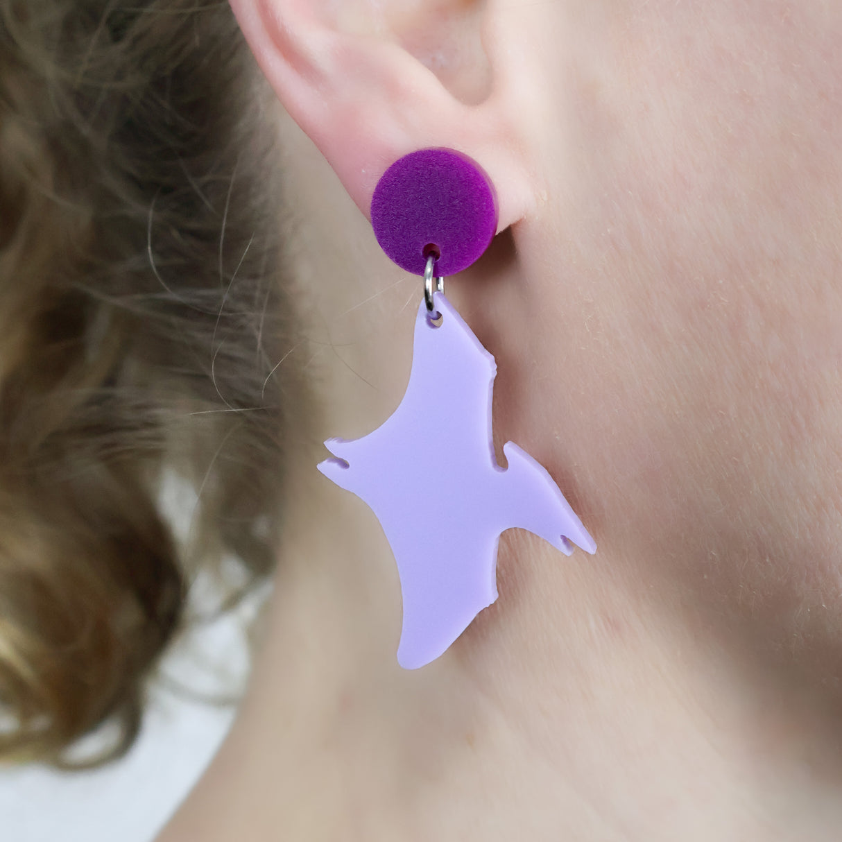 Purple pterosaur dangle earrings with darker purple toppers. Being modelled.